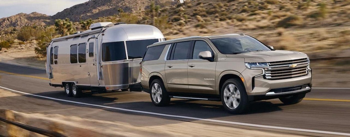 A tan 2022 Chevy Suburban towing a camper.