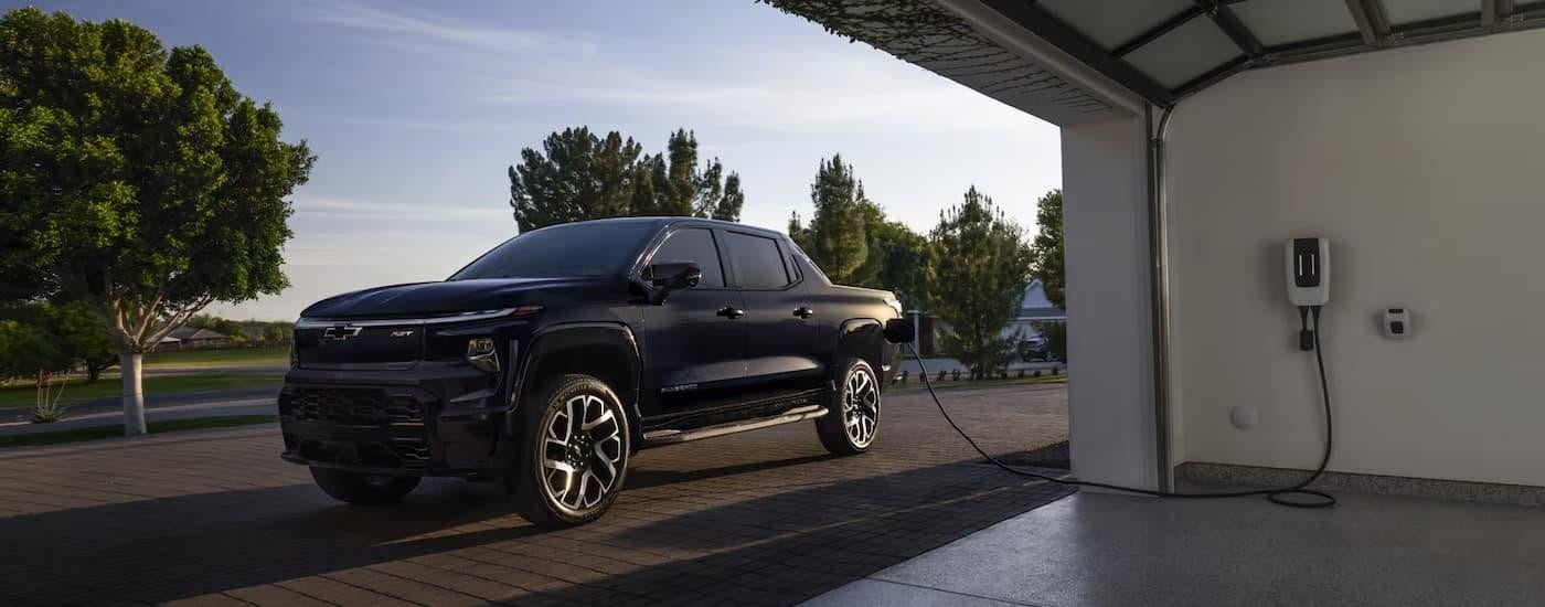 A black 2025 Chevy Silverado EV is parked outside of a garage while charging.