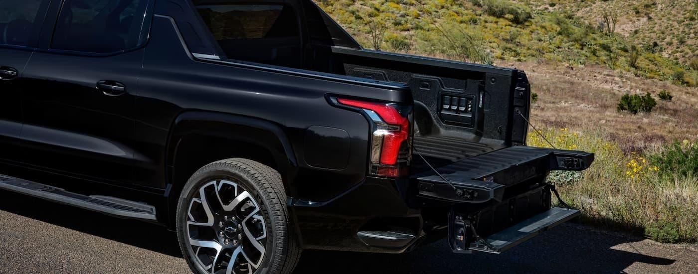 The bed and gate on a black 2025 Chevy Silverado EV is open while parked near grass.
