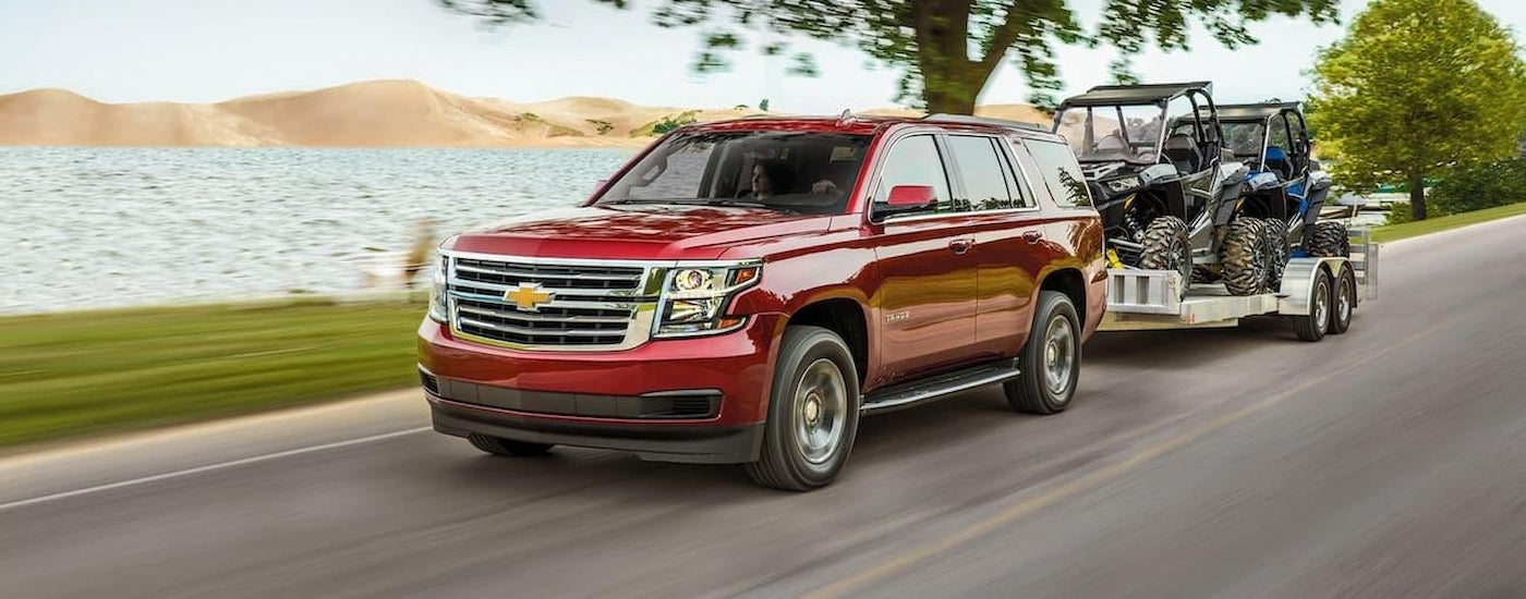 A red 2020 Chevy Tahoe towing UTVs.