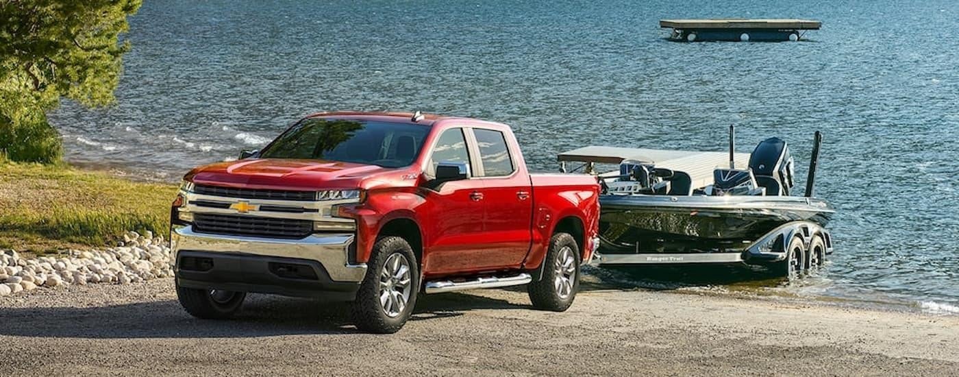 A red 2022 Chevy Silverado 1500 LTD is towing a boat out of a lake.