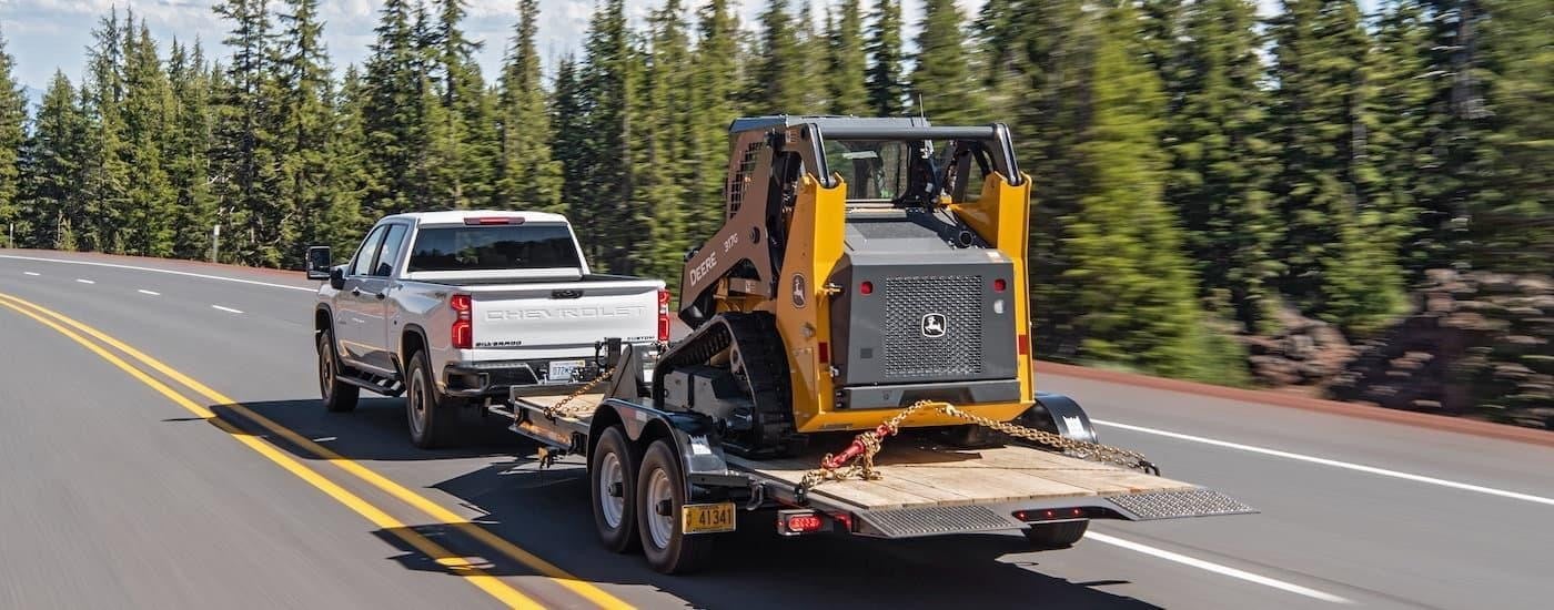 A white 2020 Chevy Silverado 2500HD towing heavy machinery.