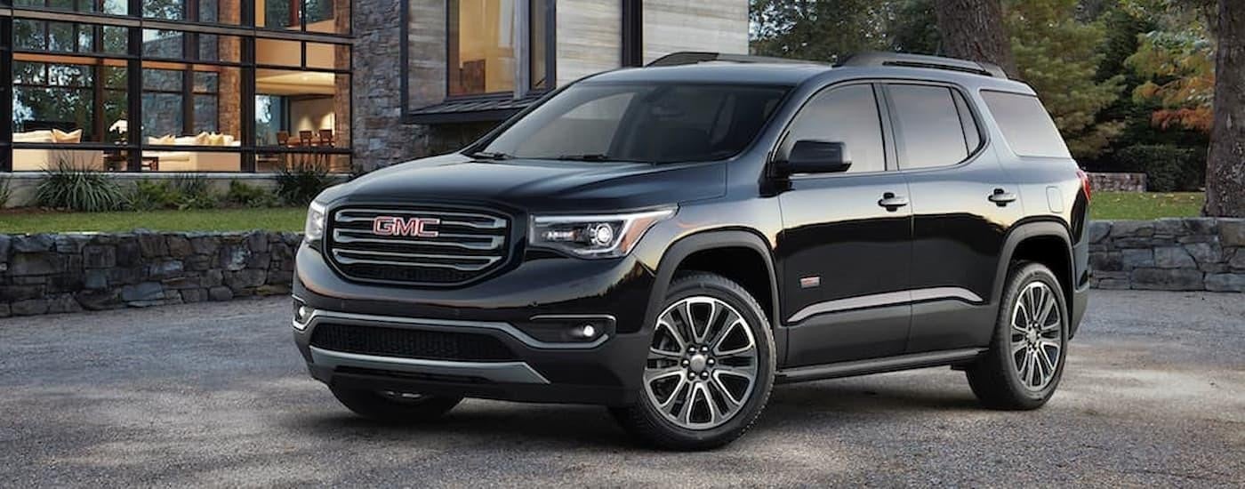A black 2019 GMC Acadia used SUV for sale is shown parked in a driveway next to a house.