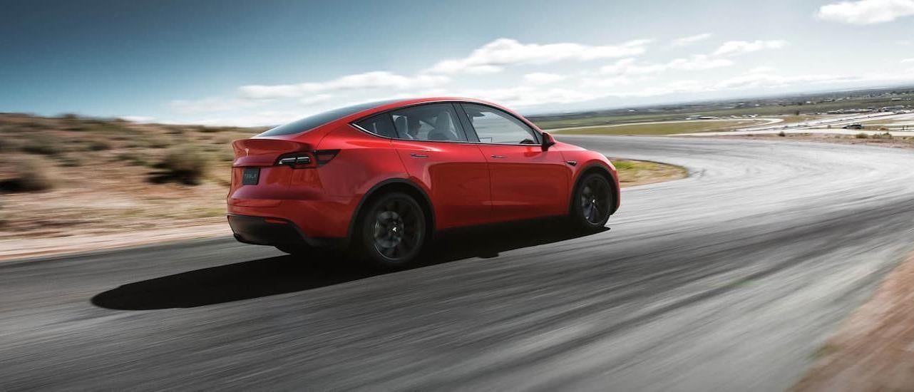 A red 2021 used Tesla Model Y is shown from the rear driving on an open road.