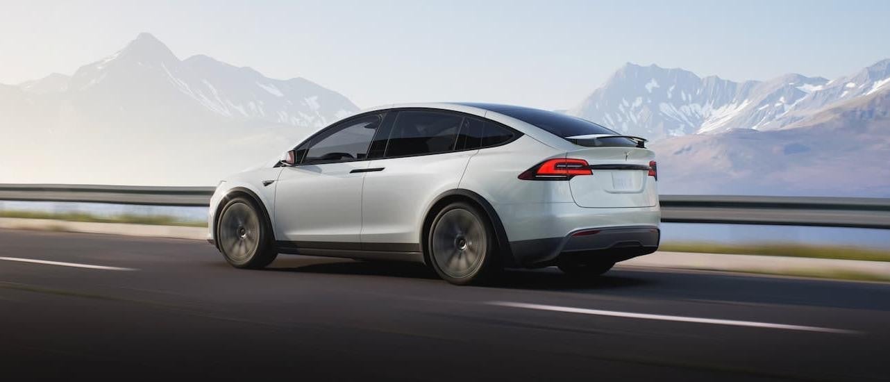 A white 2022 Tesla Model X is shown from the side driving on an open road.