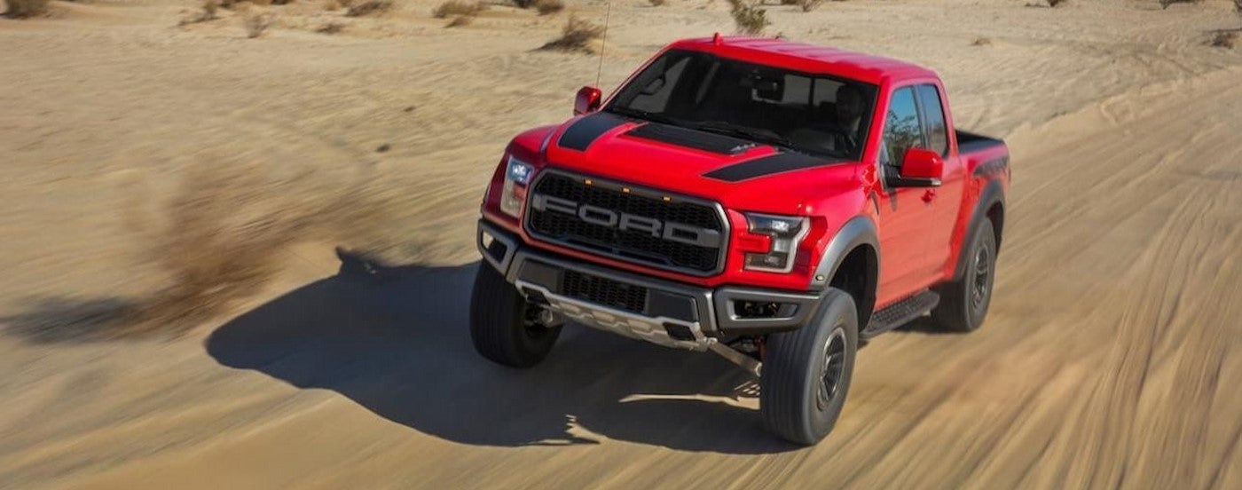 A red 2021 Ford F-150 Raptor off-roading in a desert.