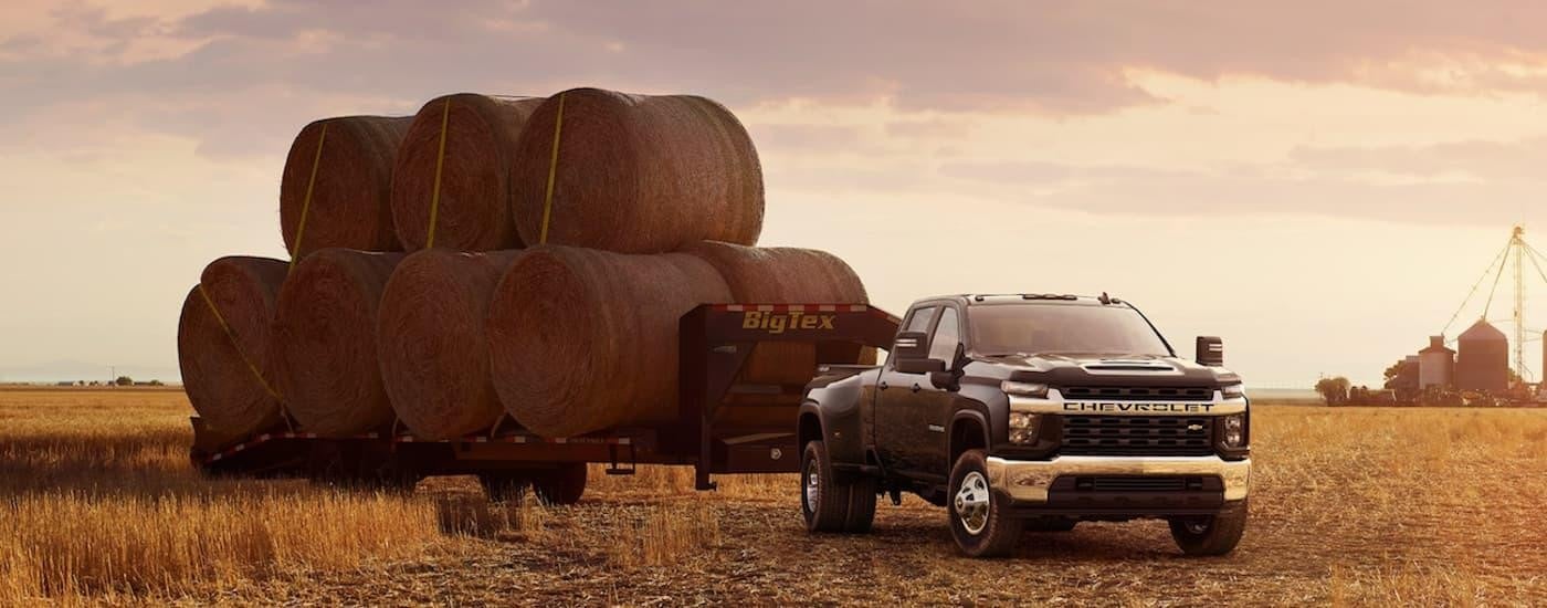 A black 2021 Chevy Silverado 3500 HD is shown parked in a field towing hay.